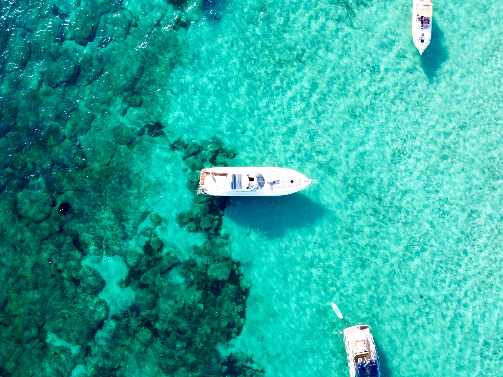 Three luxury yachts at anchor in green sea in daylight